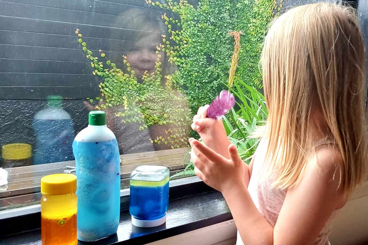 A child plays with a sensory bottle and has three others lined up on the window sill.