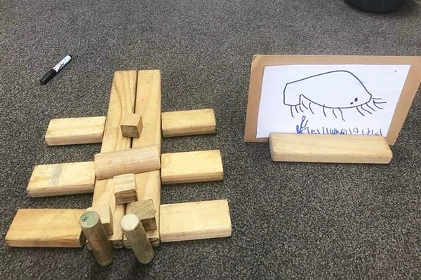 A bronze beetle made out of wooden blocks with a white board drawn sign beside it.