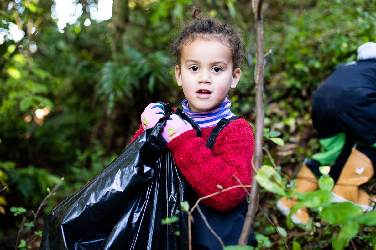 A child collecting up rubbish in the bush with a rubbish bag
